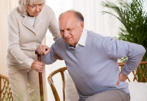 An image of an old man having trouble getting off of the couch because of his back pain.